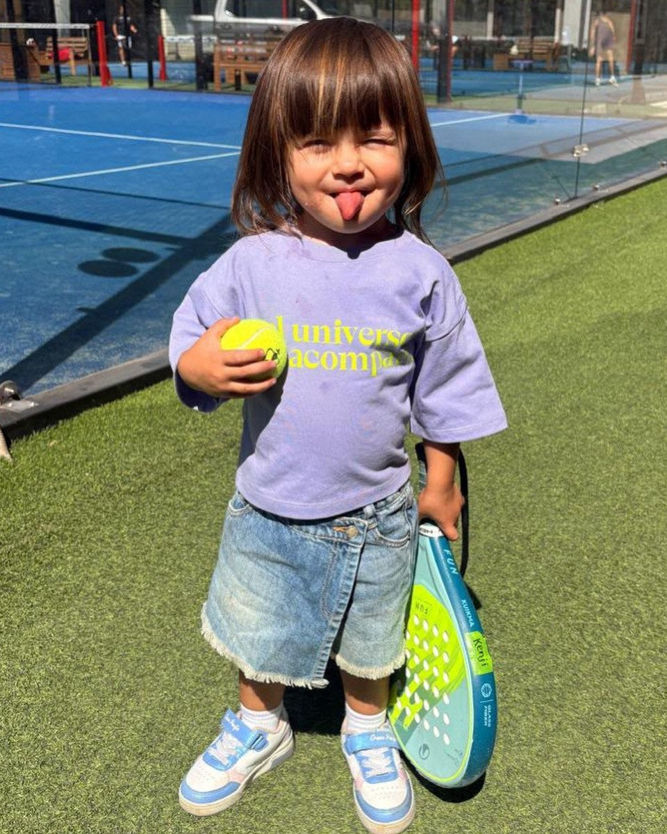 Valentina (2 a&ntilde;os) con Polera Universo talla 2, sacando la lengua con una pelota y una paleta de p&aacute;del