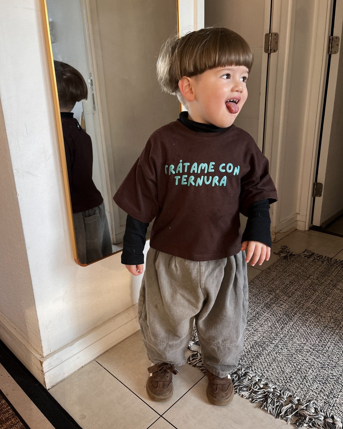 Ren (casi 3 a&ntilde;os) sacando la lengua frente a un espejo, con Polera Ternura talla 2 sobre una capa negra de cuello alto