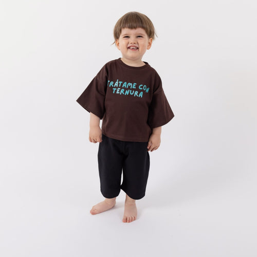 Peque de 2 años sonriendo con la Polera Ternura café oscuro talla 2 de calce oversize y pantalón negro, vista frontal