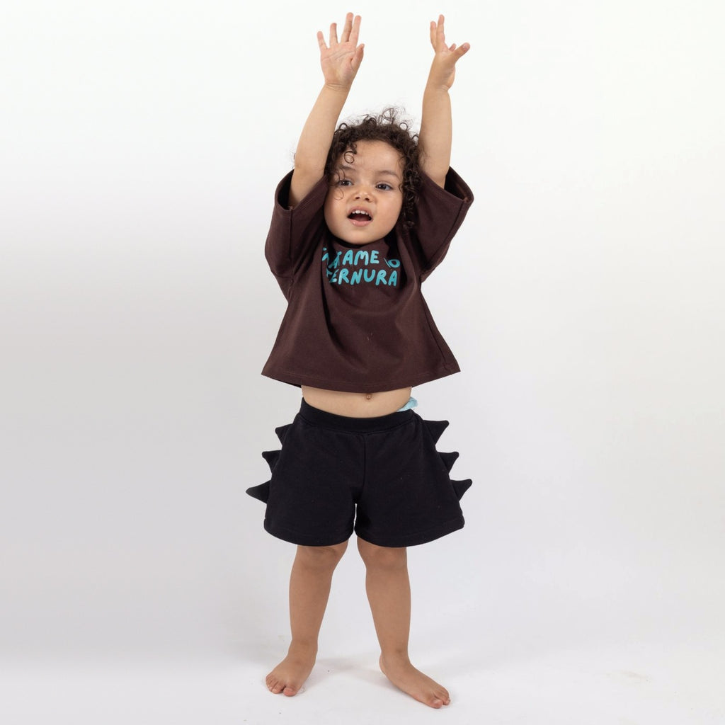 Peque de 2 años con los brazos arriba usando el Short Dinosaurio negro talla 1 y la Polera Ternura