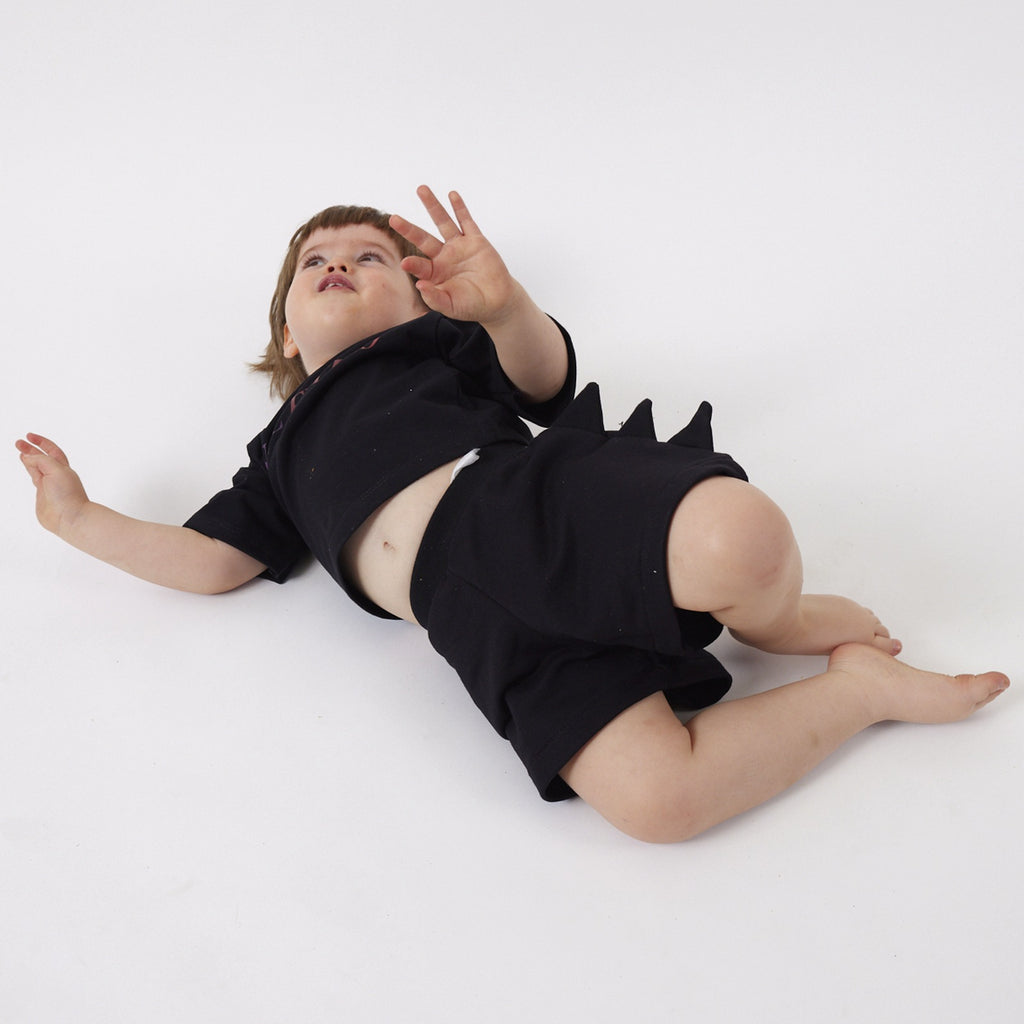 Peque de 2 años jugando en el suelo con el Short Dinosaurio negro talla 1 y la Polera Futuro