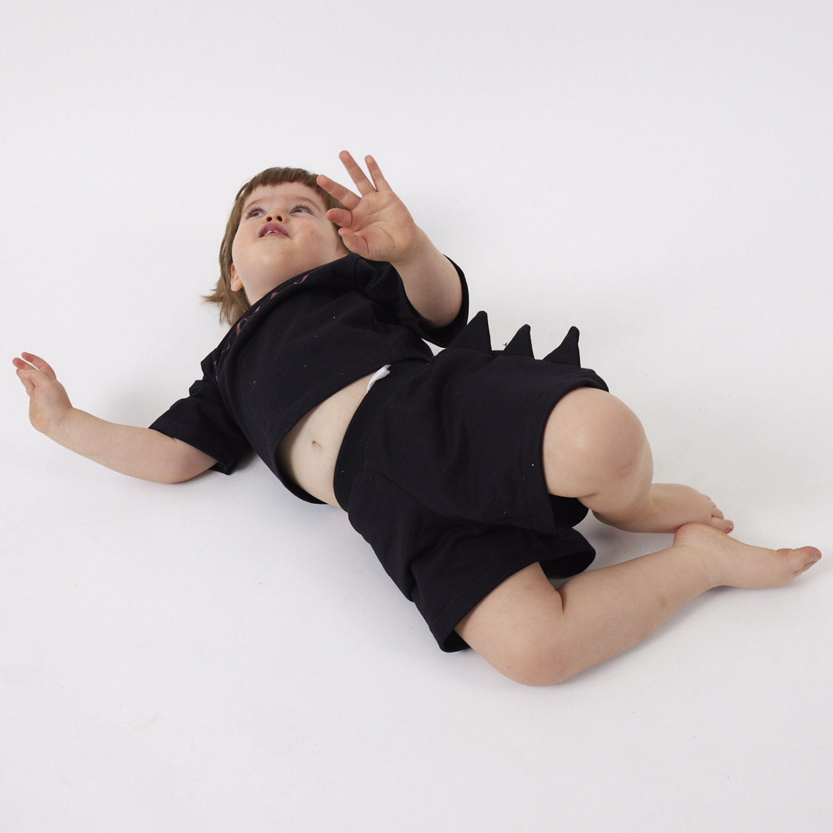Peque de 2 años jugando en el suelo con el Short Dinosaurio negro talla 1 y la Polera Futuro