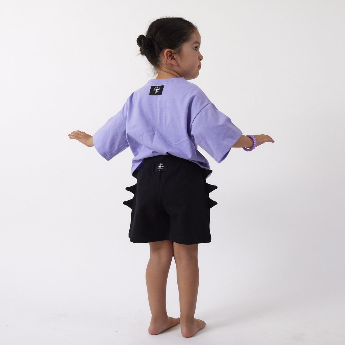 Peque de 3 años de espalda con el Short Dinosaurio talla 2 y la Polera Universo, con las etiquetas por fuera